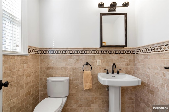 half bathroom featuring a wainscoted wall, toilet, tile walls, and a sink