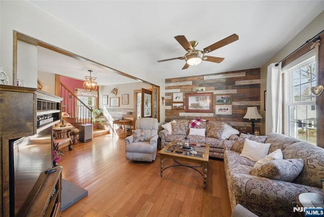 living room with wooden walls, light wood-type flooring, stairs, and an accent wall