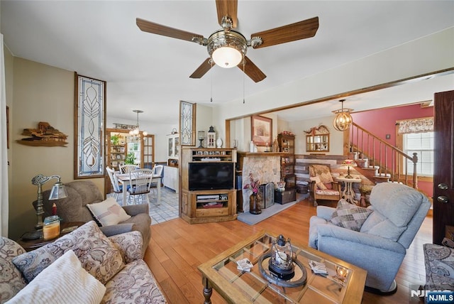 living room with stairway, a healthy amount of sunlight, ceiling fan with notable chandelier, and wood-type flooring