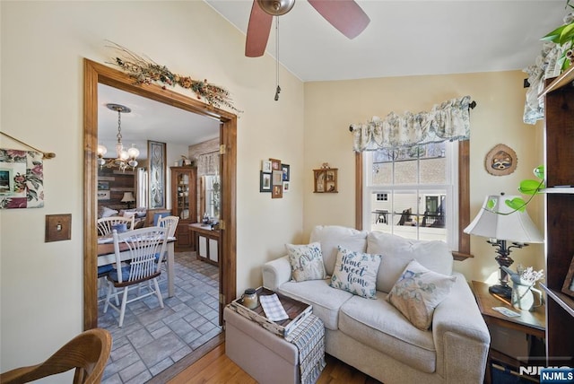 living area featuring stone tile floors and ceiling fan with notable chandelier