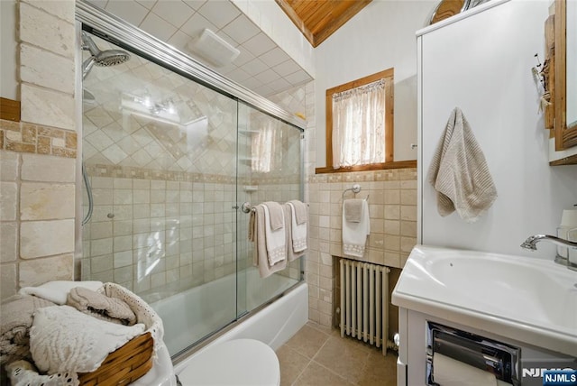 full bathroom featuring radiator heating unit, bath / shower combo with glass door, tile patterned flooring, tile walls, and toilet