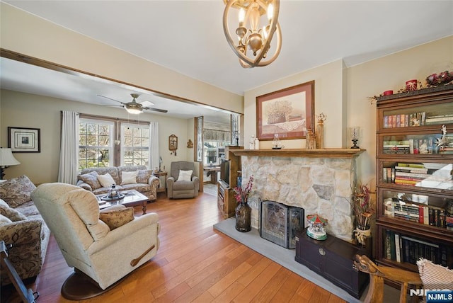 living room featuring hardwood / wood-style floors, a stone fireplace, and ceiling fan with notable chandelier