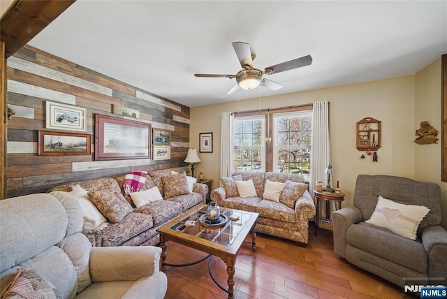 living area with an accent wall, a ceiling fan, wood walls, and wood-type flooring