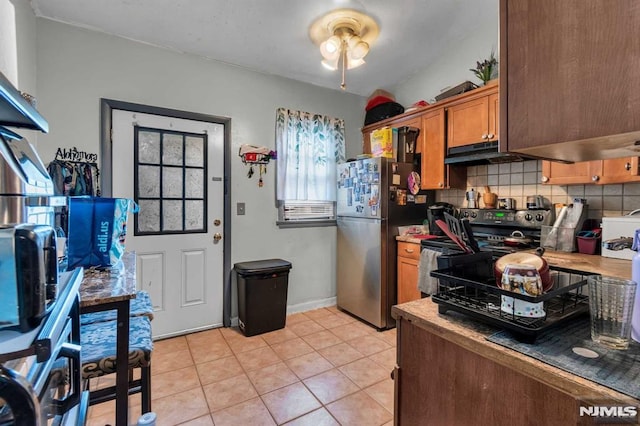 kitchen with electric stove, under cabinet range hood, tasteful backsplash, freestanding refrigerator, and light tile patterned floors