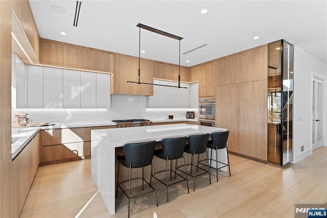 kitchen with a breakfast bar area, modern cabinets, light wood-style flooring, and a center island