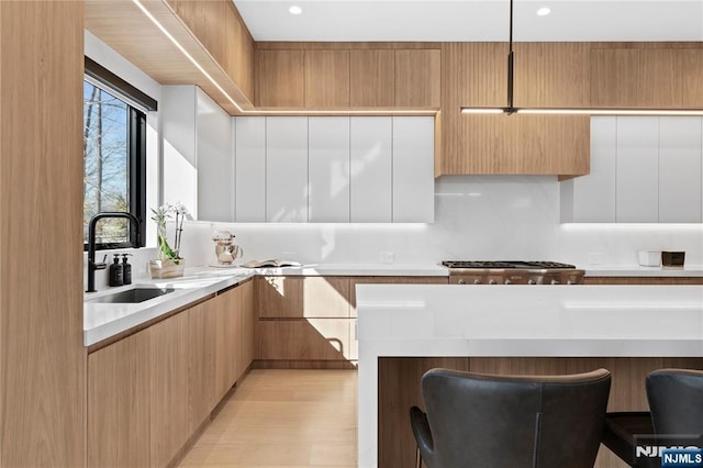 kitchen with a sink, light countertops, stainless steel gas stovetop, a kitchen breakfast bar, and modern cabinets