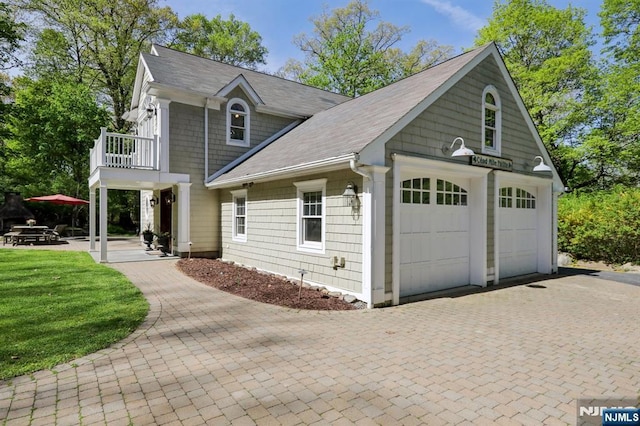 view of front of home with a garage, a balcony, a front yard, decorative driveway, and a shingled roof