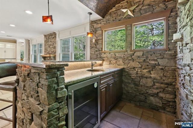 bar featuring stone tile flooring, wine cooler, a sink, vaulted ceiling, and hanging light fixtures