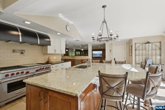 kitchen featuring decorative backsplash, lofted ceiling, ornate columns, a spacious island, and premium range