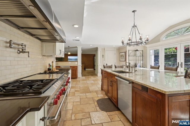 kitchen with stone tile floors, decorative columns, range hood, a sink, and appliances with stainless steel finishes