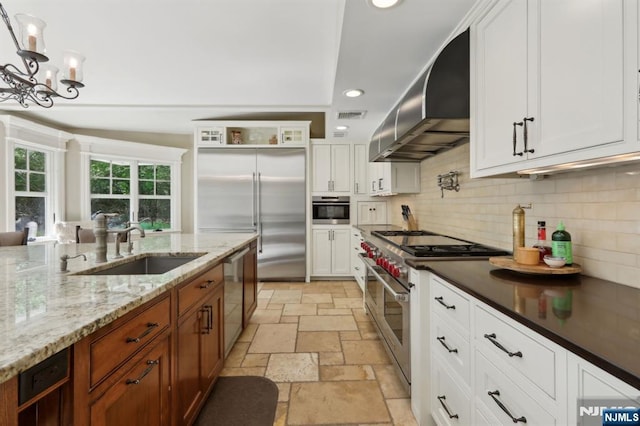 kitchen featuring wall chimney range hood, a sink, stone tile floors, high end appliances, and backsplash
