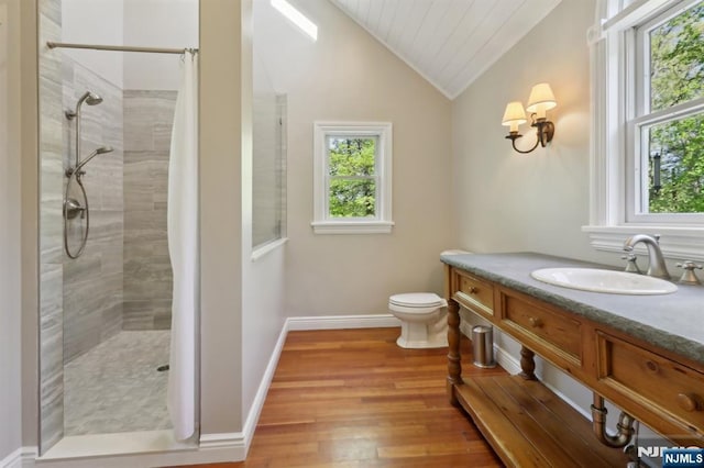 bathroom featuring vanity, wood finished floors, toilet, vaulted ceiling, and a tile shower