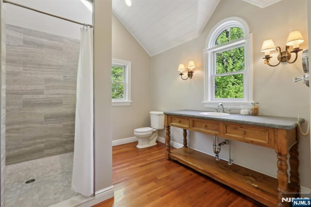 bathroom with vaulted ceiling, a tile shower, wood finished floors, baseboards, and toilet