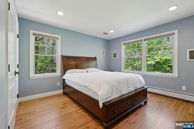 bedroom with light wood-style floors, visible vents, multiple windows, and a baseboard radiator