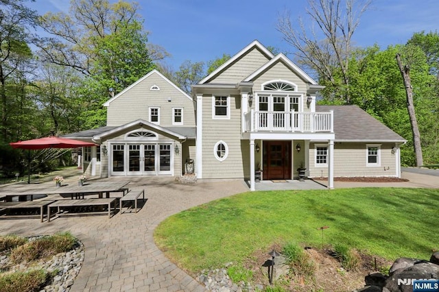 rear view of house with a lawn, a balcony, a patio area, and french doors