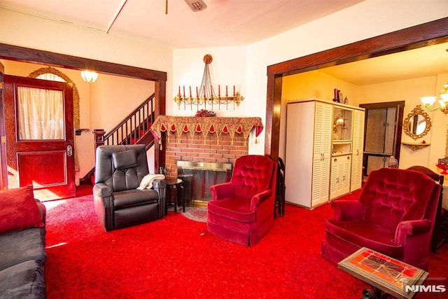 carpeted living area featuring a notable chandelier, a brick fireplace, and stairway