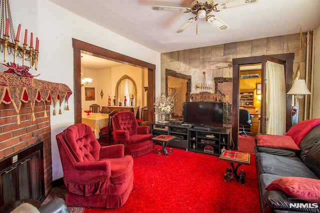 carpeted living room featuring a brick fireplace and ceiling fan with notable chandelier