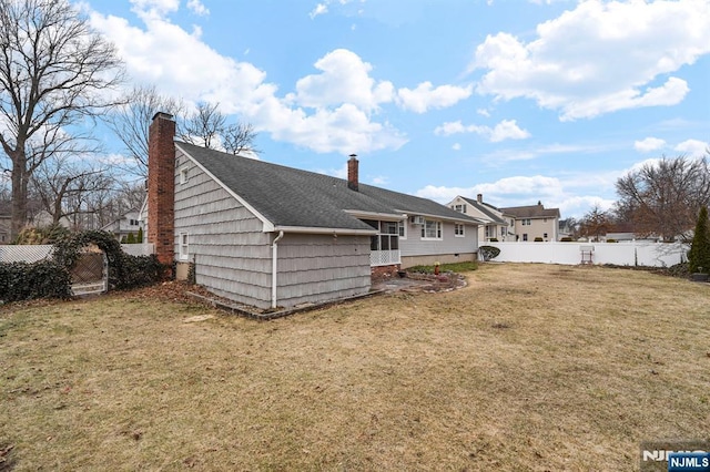 back of house with a shingled roof, a lawn, a chimney, and fence