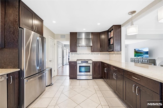 kitchen with dark brown cabinetry, light stone counters, decorative backsplash, appliances with stainless steel finishes, and wall chimney exhaust hood