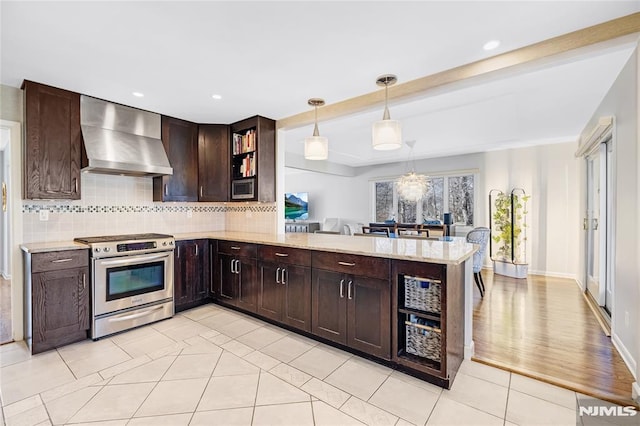 kitchen with stainless steel range with electric stovetop, dark brown cabinetry, wall chimney range hood, decorative backsplash, and hanging light fixtures