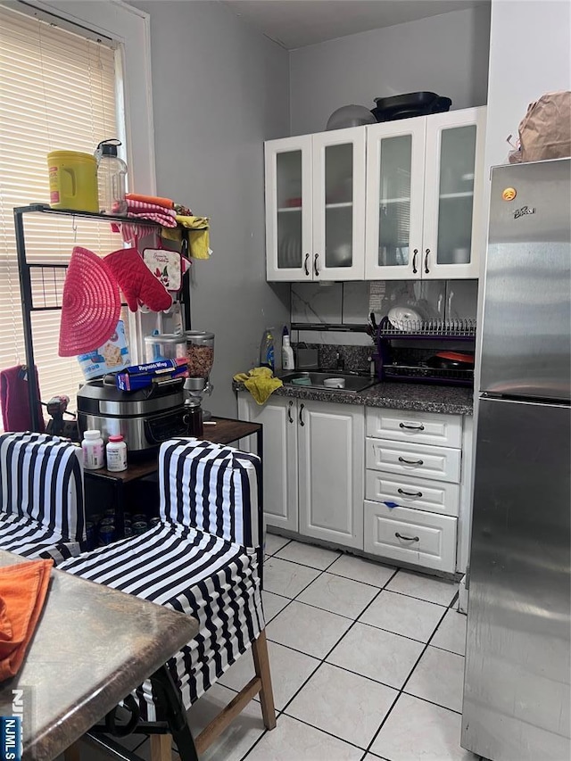 kitchen featuring glass insert cabinets, light tile patterned flooring, white cabinets, and freestanding refrigerator