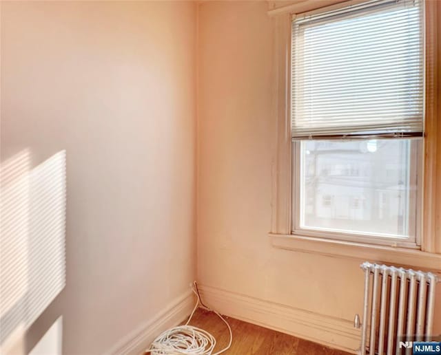 spare room with radiator, baseboards, and wood finished floors