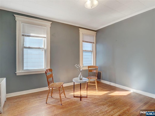 living area with crown molding, light wood-style flooring, radiator heating unit, and baseboards