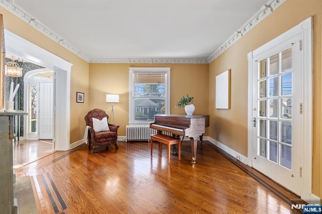 sitting room with radiator, wood finished floors, baseboards, and ornamental molding