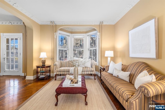 living room featuring arched walkways, crown molding, baseboards, and wood finished floors