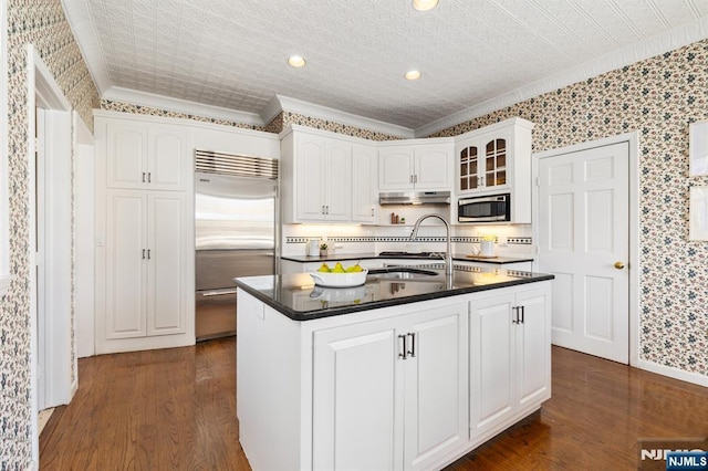 kitchen featuring under cabinet range hood, an ornate ceiling, dark countertops, white cabinetry, and built in appliances