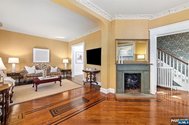 living area featuring wood finished floors, arched walkways, a fireplace, crown molding, and stairs