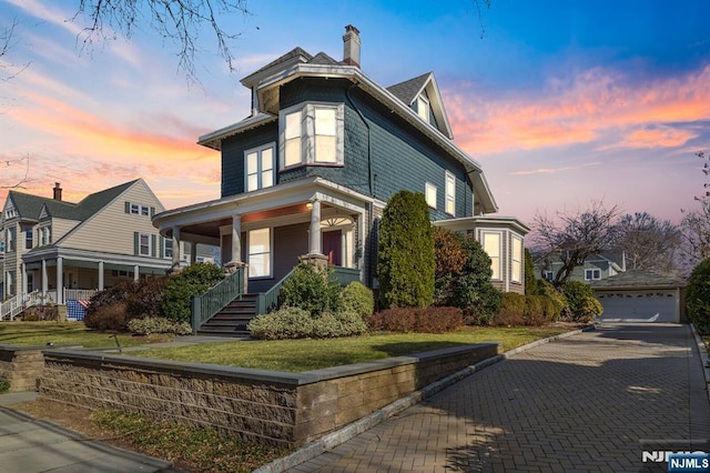 view of front of house with a detached garage, a porch, an outdoor structure, a front yard, and a chimney