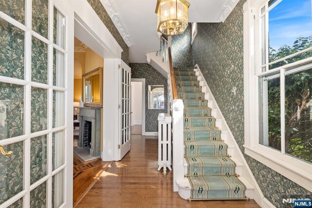 stairway featuring wallpapered walls, a notable chandelier, wood finished floors, and a fireplace with raised hearth