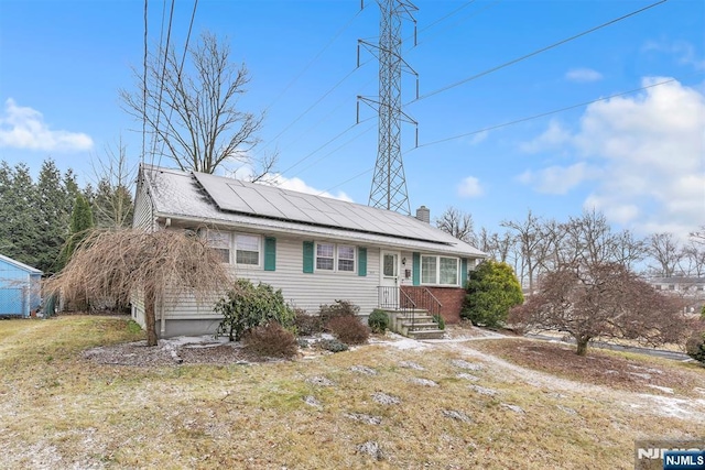 single story home with roof mounted solar panels, a chimney, and a front yard