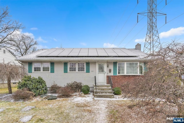 view of front of house featuring brick siding, solar panels, and a chimney