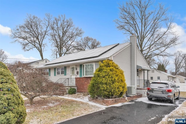 view of front of house featuring central AC unit, brick siding, roof mounted solar panels, and a chimney