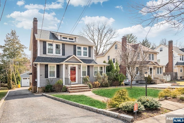 american foursquare style home featuring an outbuilding, a front yard, a chimney, a shingled roof, and a residential view