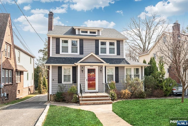 view of front facade featuring a front yard, aphalt driveway, roof with shingles, and a chimney