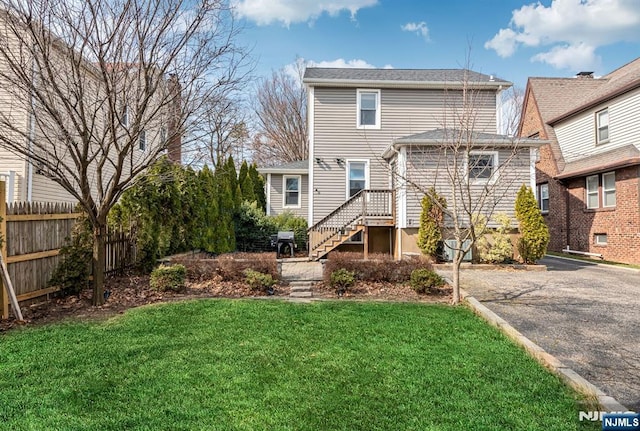 rear view of property featuring a yard, driveway, and fence