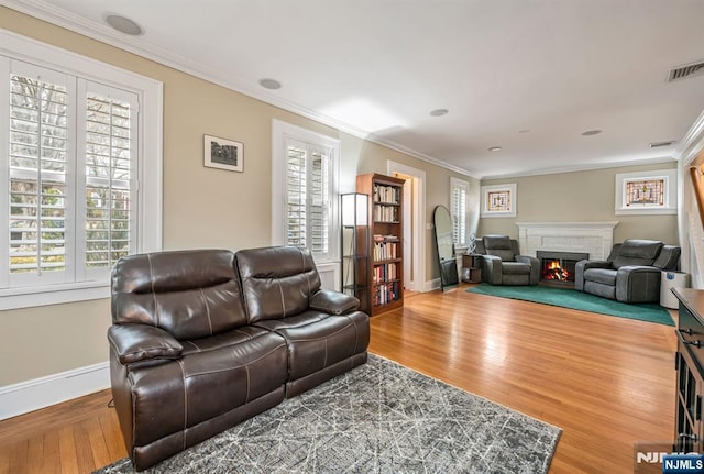 living area with a wealth of natural light, visible vents, a brick fireplace, and ornamental molding