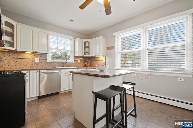 kitchen with glass insert cabinets, a kitchen bar, baseboard heating, white cabinets, and stainless steel appliances