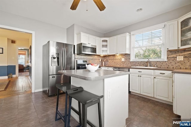 kitchen featuring a breakfast bar area, a sink, glass insert cabinets, appliances with stainless steel finishes, and backsplash