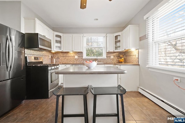 kitchen with decorative backsplash, stainless steel appliances, tile patterned flooring, glass insert cabinets, and baseboard heating