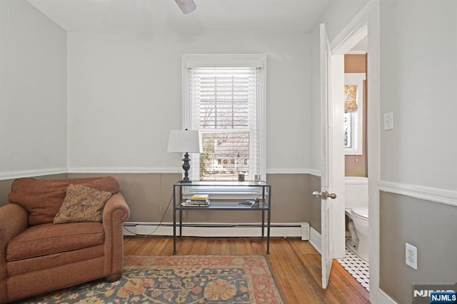 living area with baseboard heating, wood finished floors, and a ceiling fan