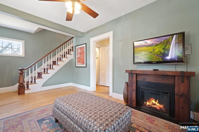 interior space featuring a glass covered fireplace, ceiling fan, baseboards, and wood finished floors