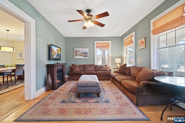 living room with light wood finished floors, a glass covered fireplace, a ceiling fan, and baseboards