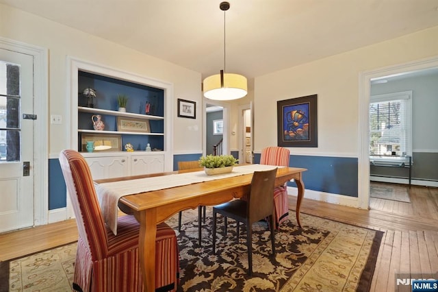 dining room featuring built in shelves, a baseboard heating unit, baseboards, and hardwood / wood-style floors