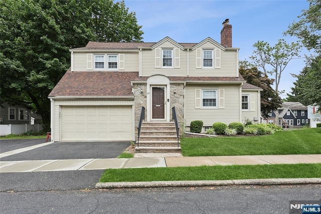 view of front of property with driveway, roof with shingles, a front yard, a garage, and a chimney