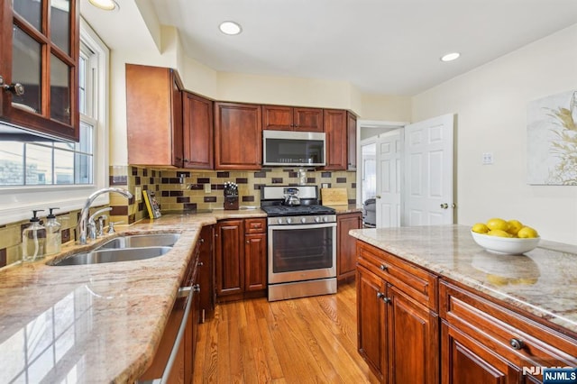 kitchen featuring tasteful backsplash, light stone countertops, light wood-type flooring, appliances with stainless steel finishes, and a sink