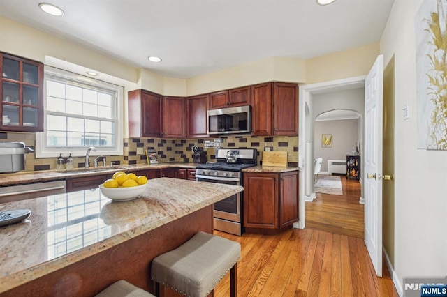 kitchen featuring backsplash, light wood-style floors, arched walkways, and appliances with stainless steel finishes